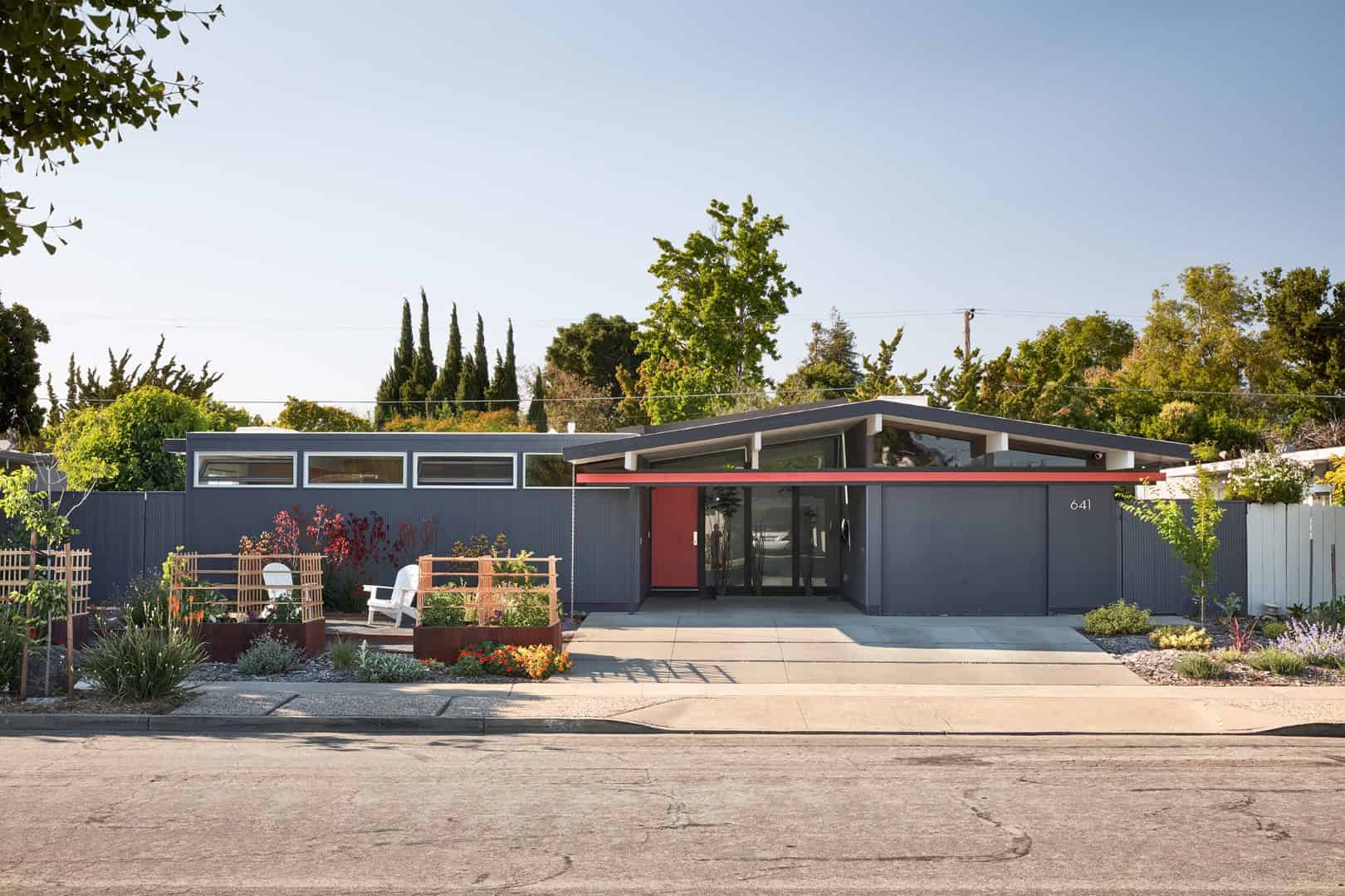 Modern mid-century single-story house with flat roof, large glass windows, and a vibrant exterior. Nature-inspired landscaping complements contemporary architecture and curb appeal.