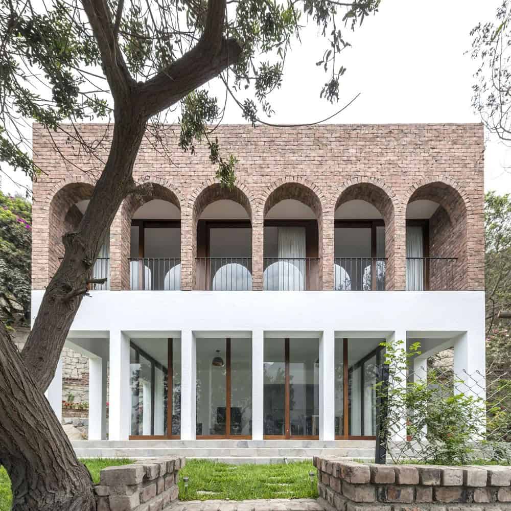 Modern multilevel house with brick and white concrete facade, arched windows, and lush front garden, showcasing contemporary architecture design.