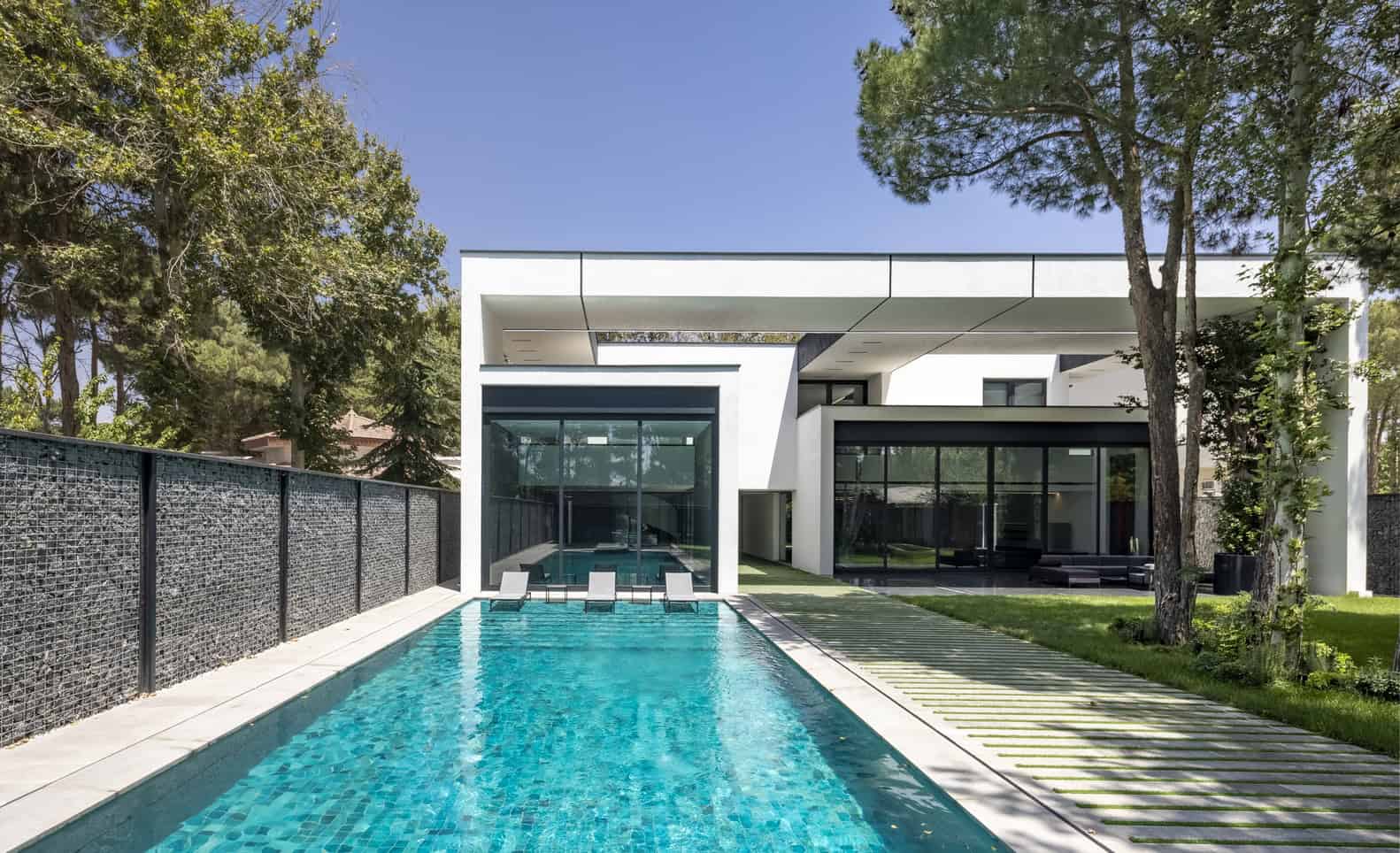 Contemporary modern house with sleek white exterior, large glass windows, and a luxurious swimming pool, set amidst lush greenery and tall trees, showcasing innovative architecture design.