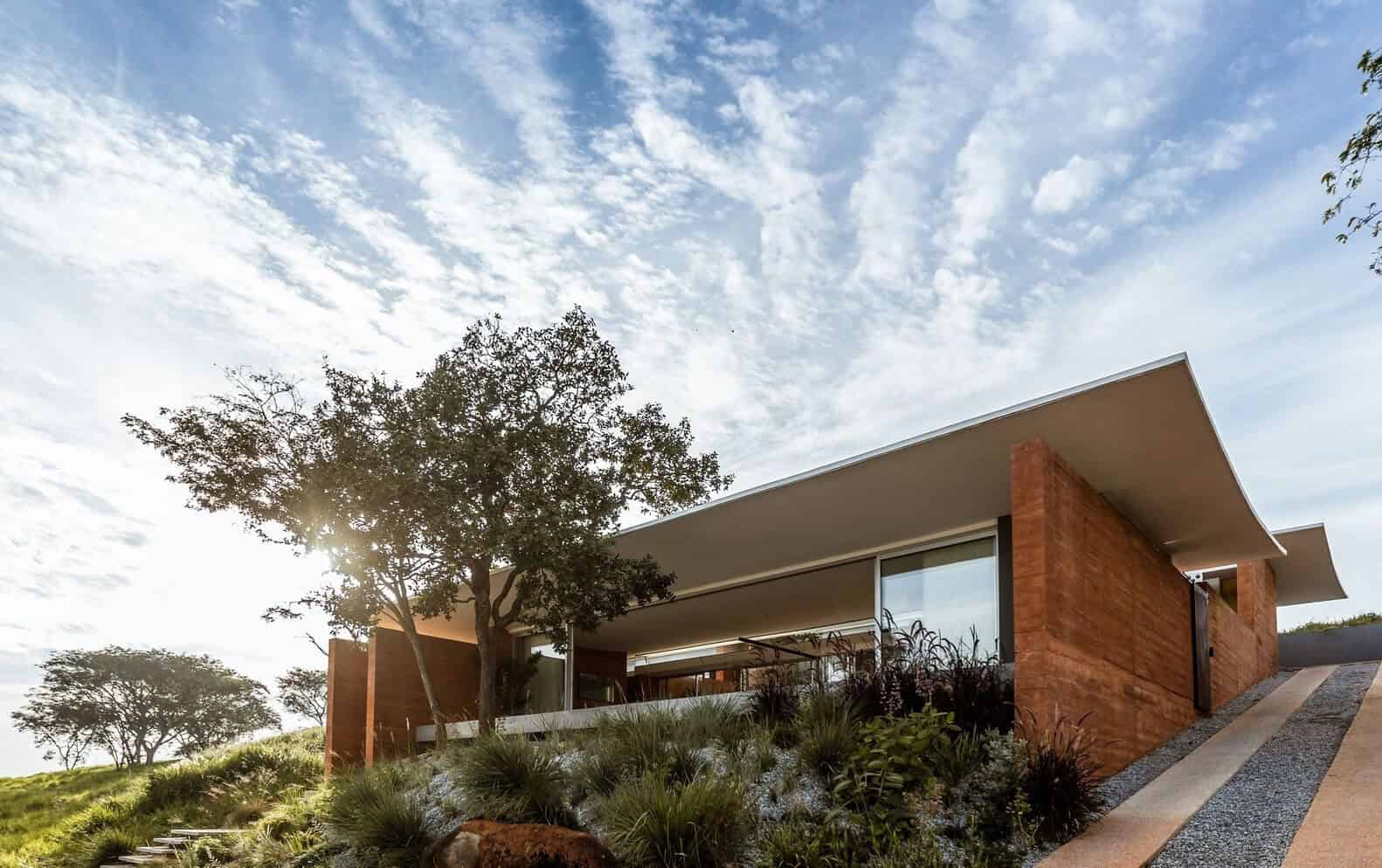 Contemporary modern house with sleek design, large glass windows, flat roof, surrounded by natural landscaping and a clear sky in the background.