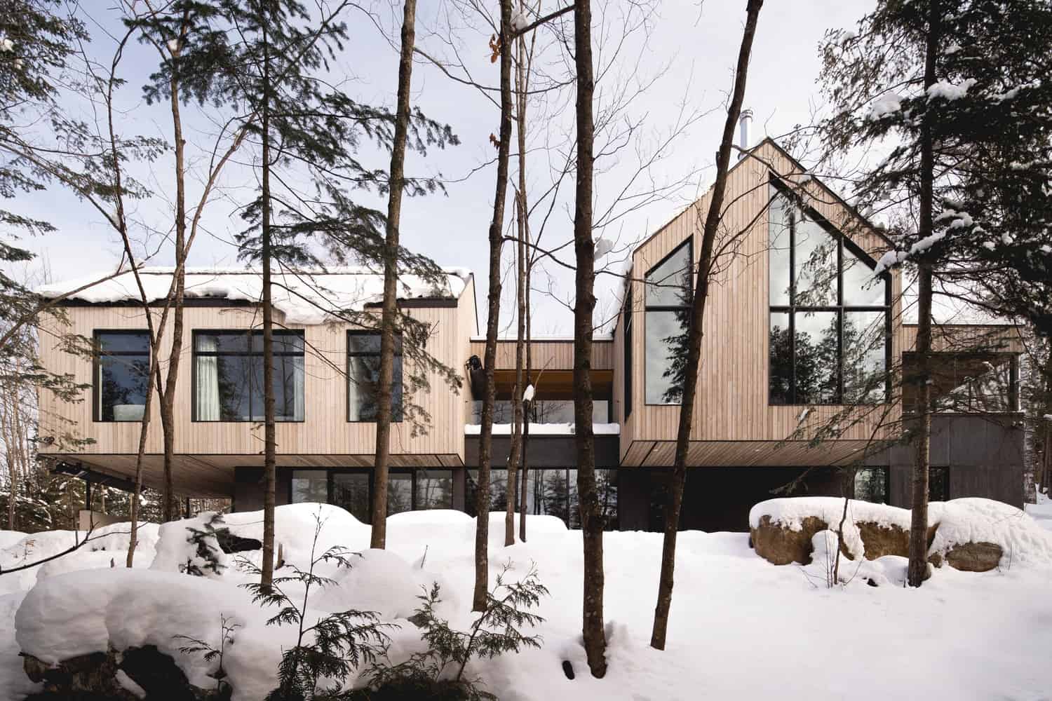 Contemporary wooden house surrounded by snow-covered trees in winter, showcasing modern architecture, minimalist design, and eco-friendly construction in a forest setting.