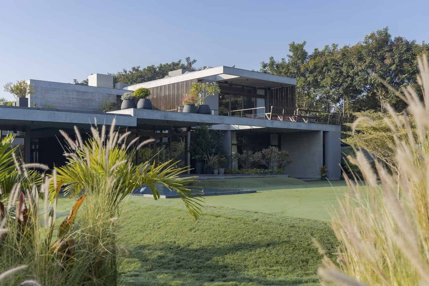 Modern contemporary house with sleek architectural design and large glass windows, surrounded by lush greenery and landscaped gardens, showcasing minimalist and outdoor living spaces.