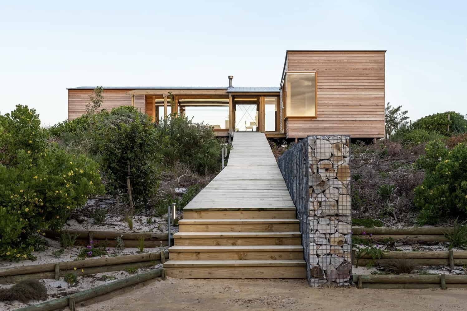 Contemporary wooden house on hillside with eco-friendly design, modern architecture, and natural materials. Features a wooden staircase leading to a minimalist home with large windows and lush landscaping.