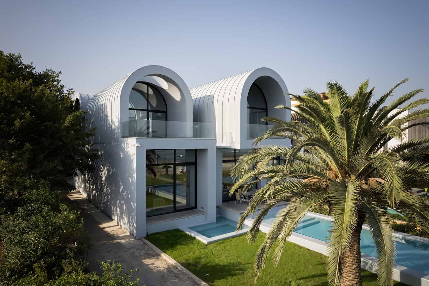 Futuristic modern house with curved white architectural design, large glass windows, outdoor pool, and lush landscaping, exemplifying innovative architecture and contemporary home design.