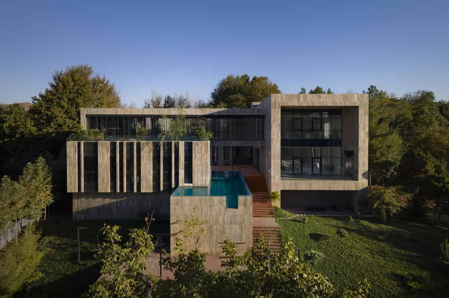 Contemporary modern house with striking architecture, extensive glass windows, and a sleek design nestled among greenery.