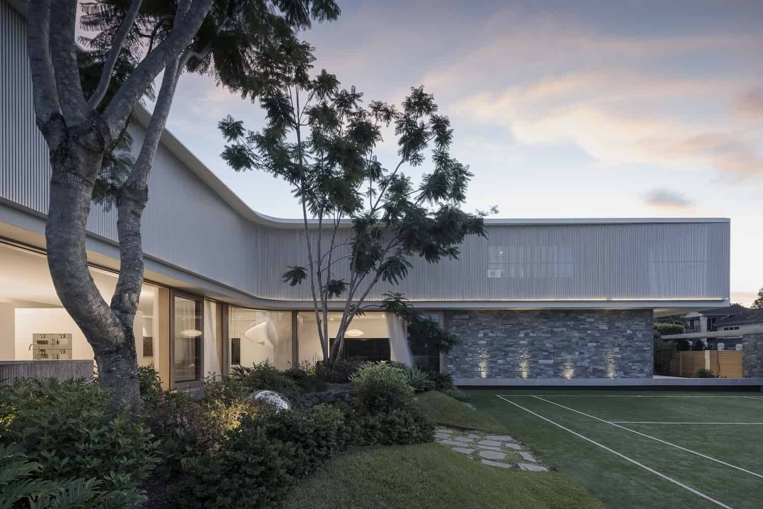 Contemporary modern house with sleek architectural design, stone accent wall, large glass windows, and lush landscaping, showcasing innovative architecture and stylish design.