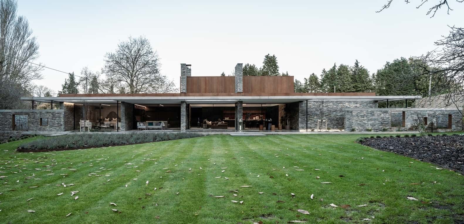 Modern luxury house with extensive use of natural stone, wood, and glass, featuring a spacious outdoor area and contemporary architectural design.