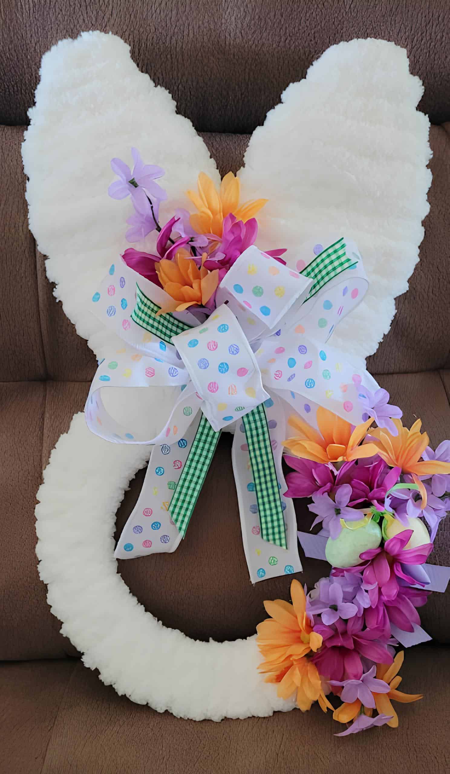 15. Fuzzy Bunny Wreath DIY Easter bunny wreath with fluffy white ears and base, accented with colorful spring flowers, green gingham and Easter egg print ribbons – festive Dollar Tree-inspired front door decor.