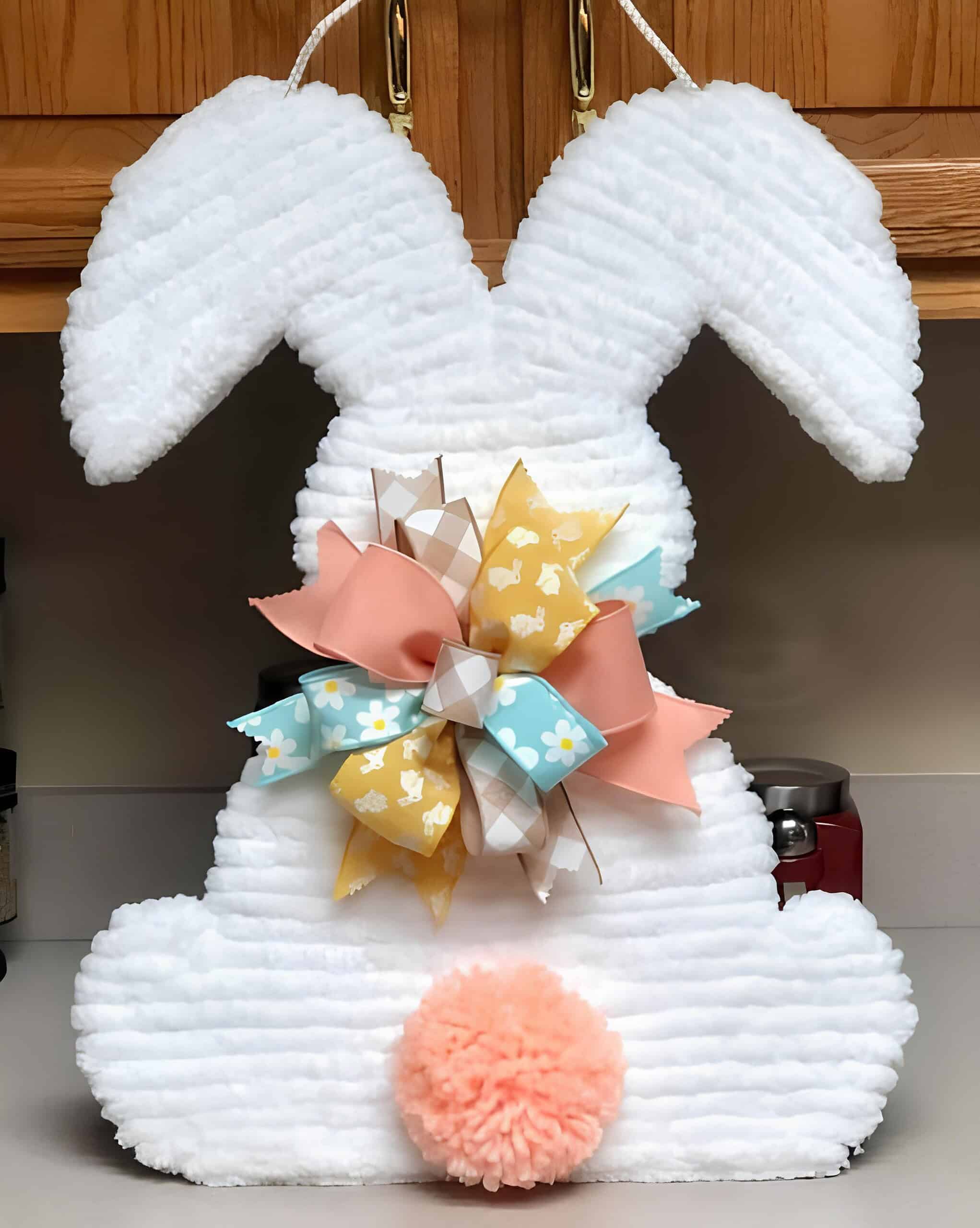 7. Easter Bunny Wreath DIY bunny butt Easter door hanger made with white chenille fabric, colorful spring ribbon bow, and a fluffy peach pom-pom tail – cute and whimsical Dollar Tree Easter craft.