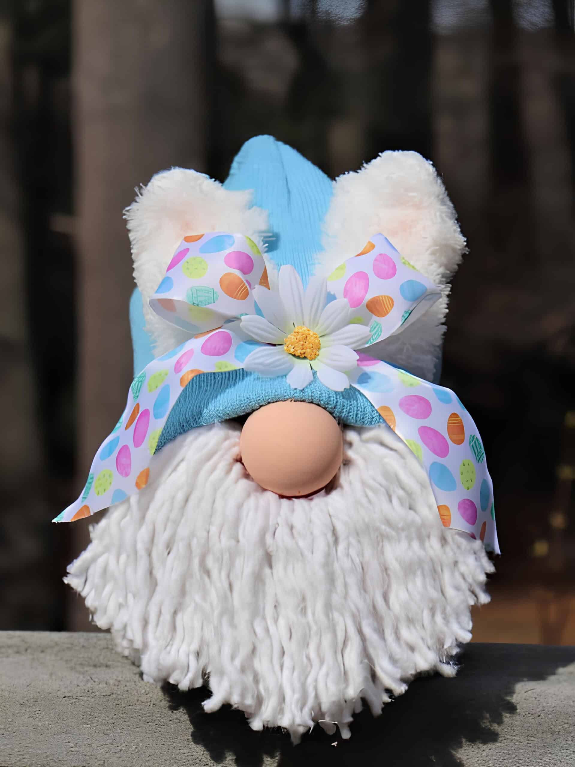 14. Easter Bunny Gnome DIY using Dollar Tree supplies DIY Easter gnome with a blue hat, fluffy white bunny ears, faux fur beard, peach-colored nose, and a colorful egg-patterned bow with a white daisy – whimsical Dollar Tree spring craft decor.
