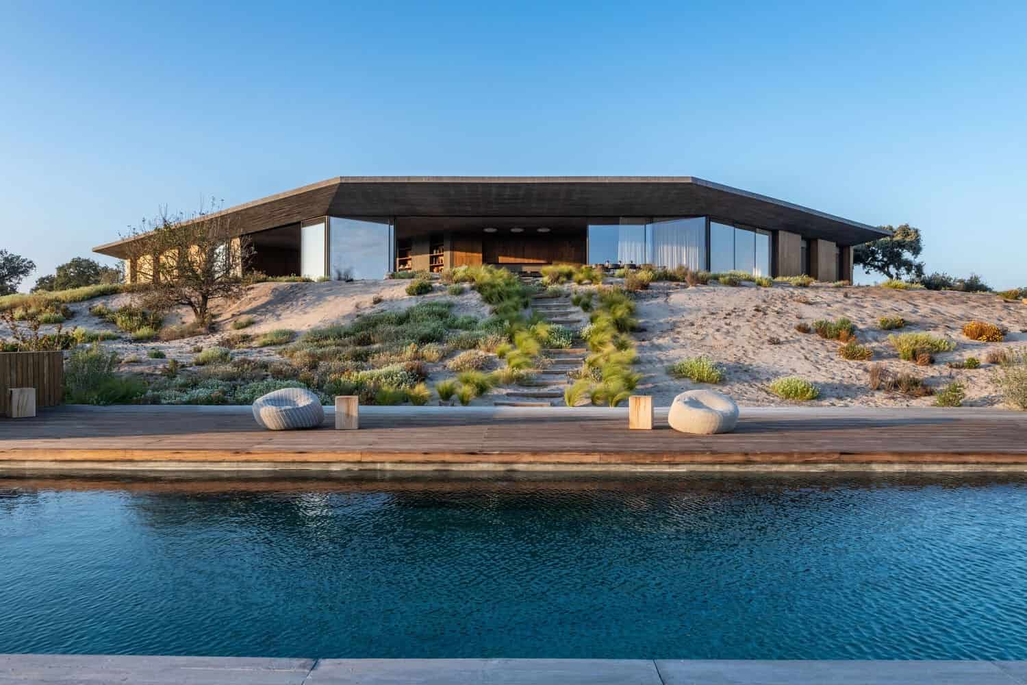 Modern contemporary house with seamless indoor-outdoor living, featuring a sleek design and large glass windows set on a sandy landscape, perfect for luxury estate living.