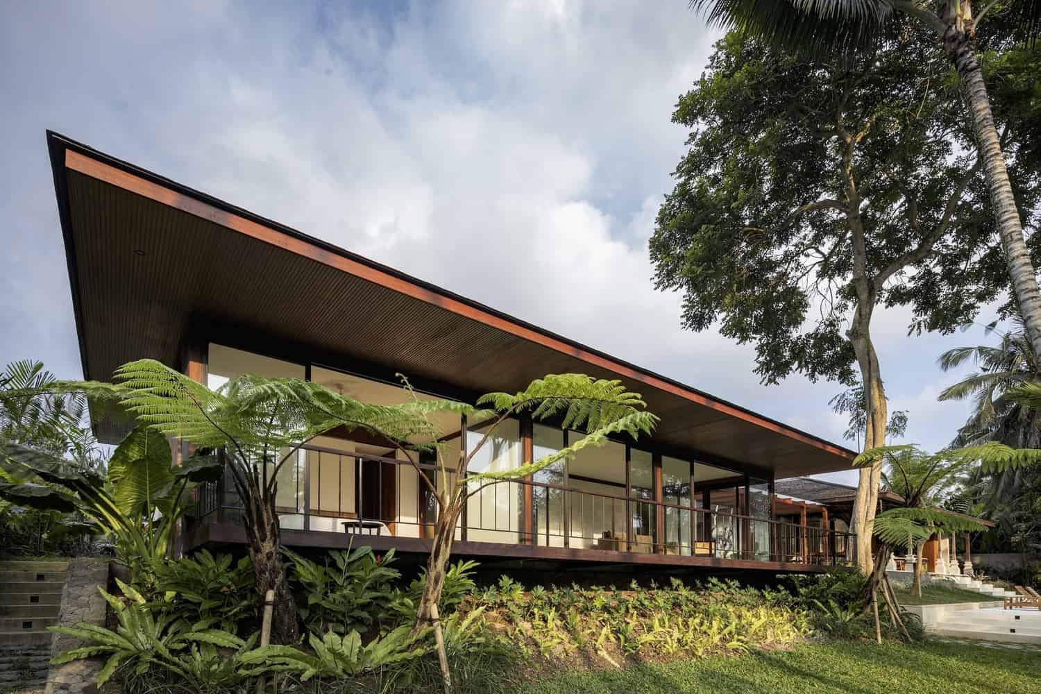 Modern tropical house with open glass walls, lush greenery, and sleek design.