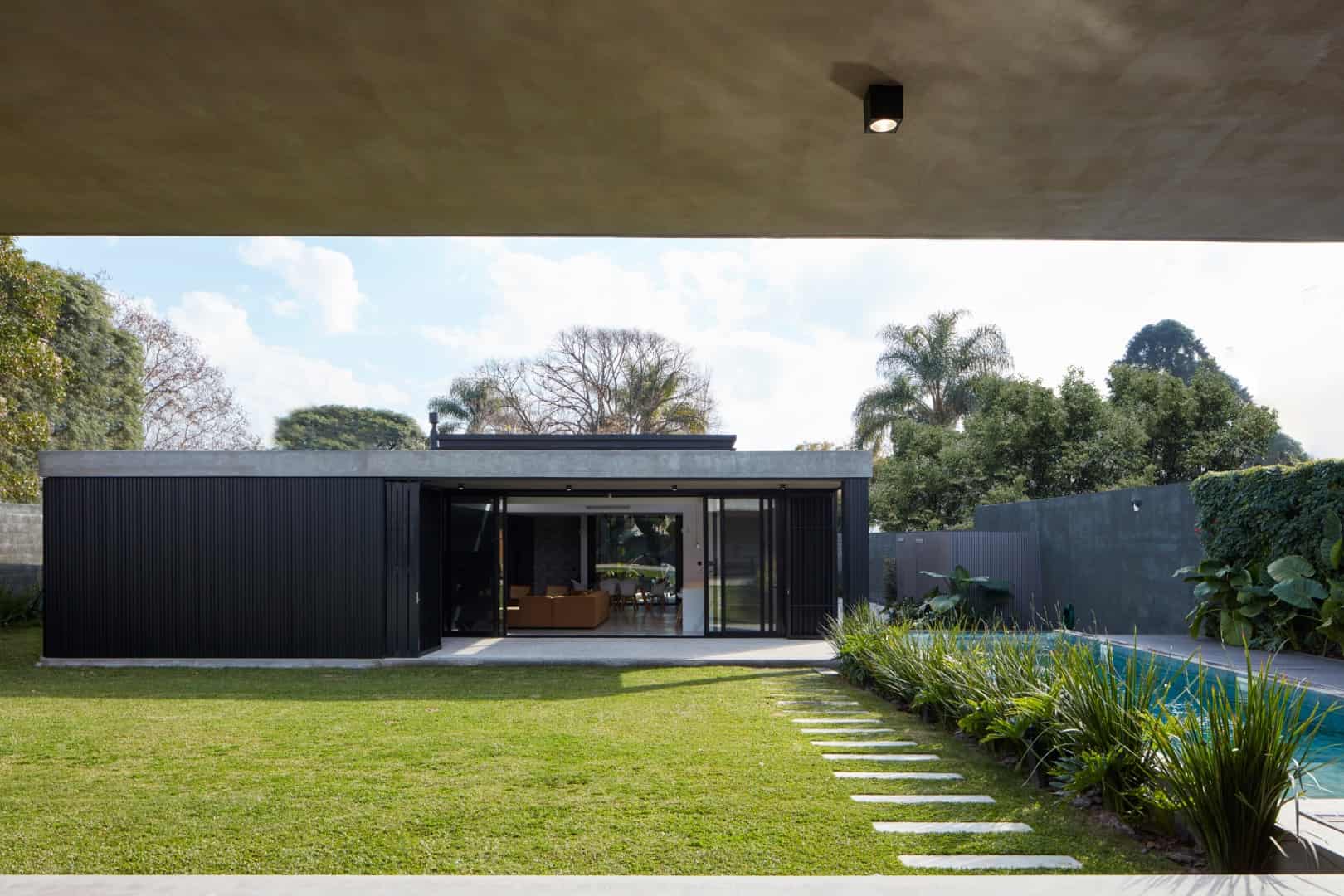 Contemporary modern house with sleek black exterior, large glass sliding doors, lush green lawn, and swimming pool, showcasing minimalist architecture and stylish outdoor living space.