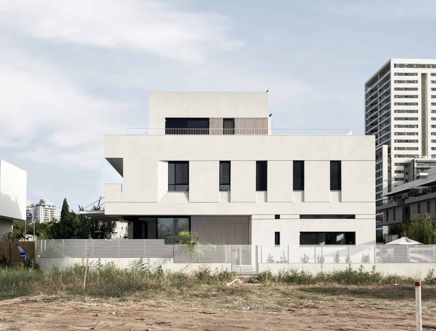 Modern minimalist white residential building with clean lines and large windows, surrounded by urban high-rise structures and outdoor landscape.