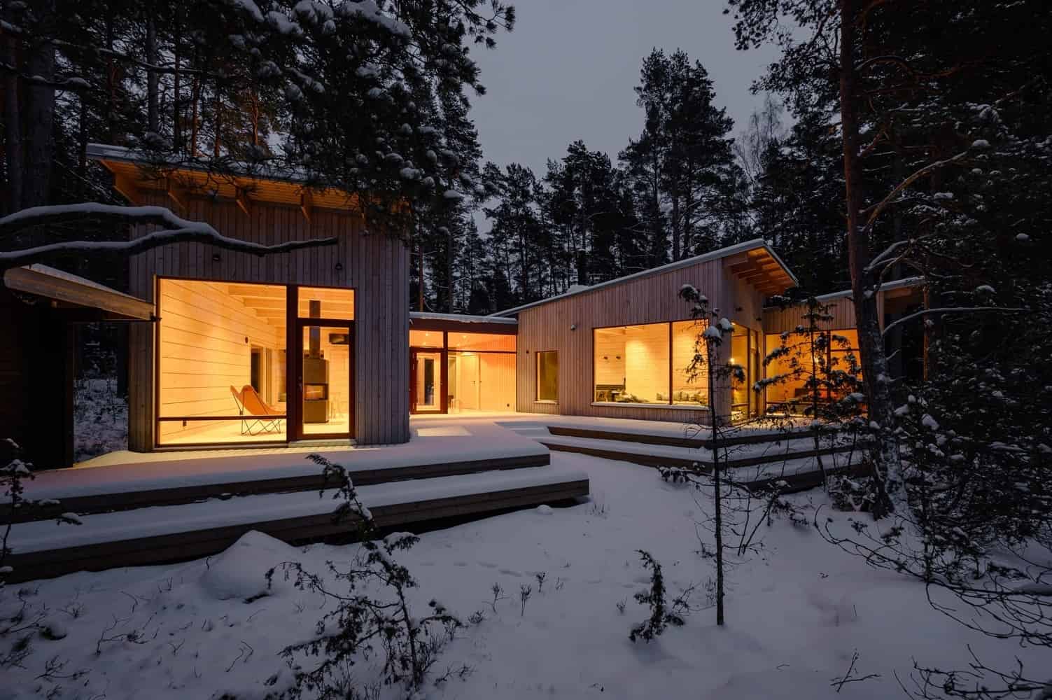 Two Sisters Holiday Home / MNY Arkitekter / Finland Contemporary wooden cabin architecture in snowy forest setting with large glass windows and warm interior lighting, modern mountain retreat design by Architecture Art Designs.