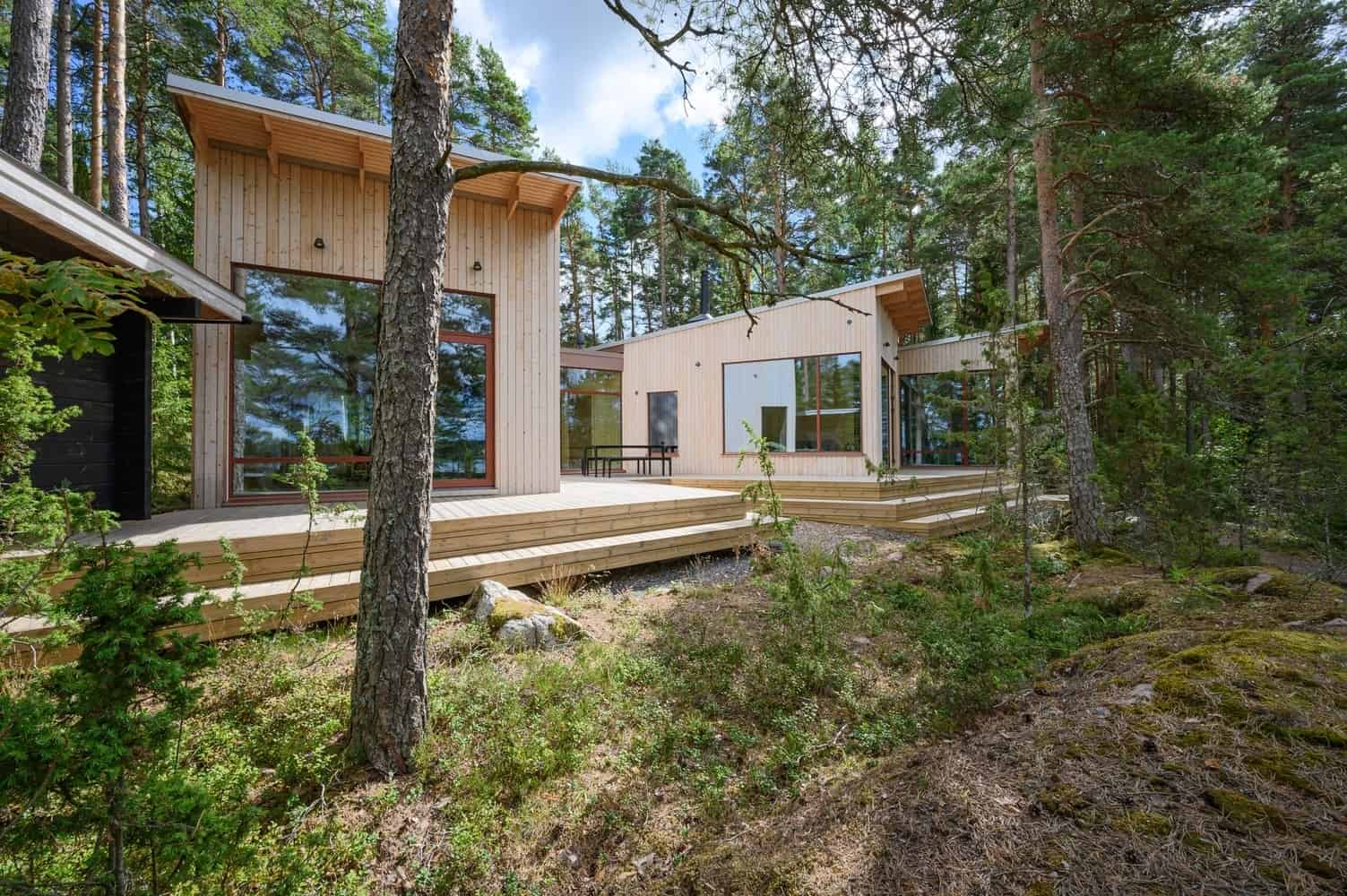 Modern minimalist wooden house with large glass windows surrounded by tall pine trees in a forest setting for eco-friendly and sustainable architecture.