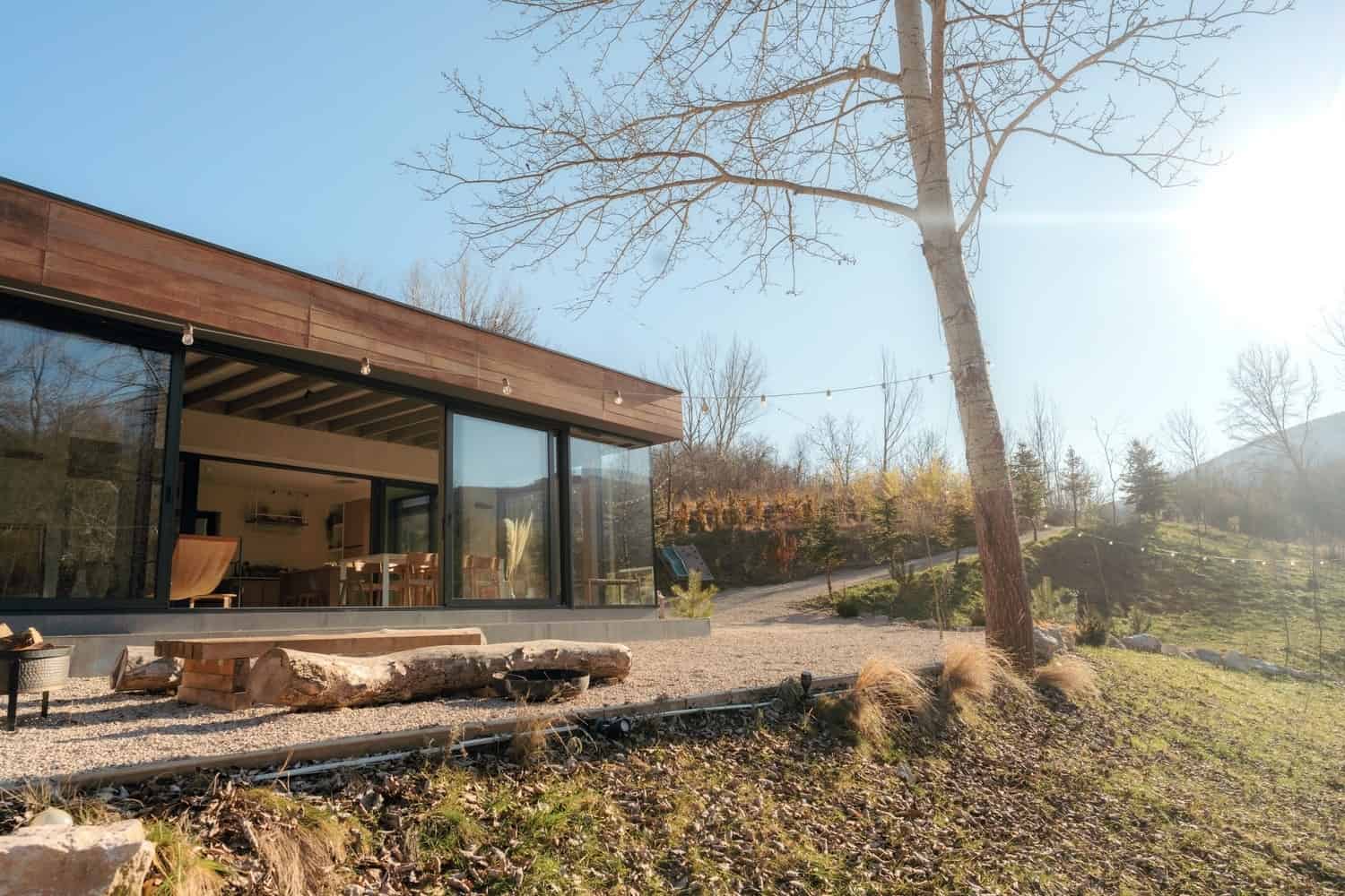 Modern minimalist house with large glass windows and wooden accents in a scenic outdoor setting during daytime.