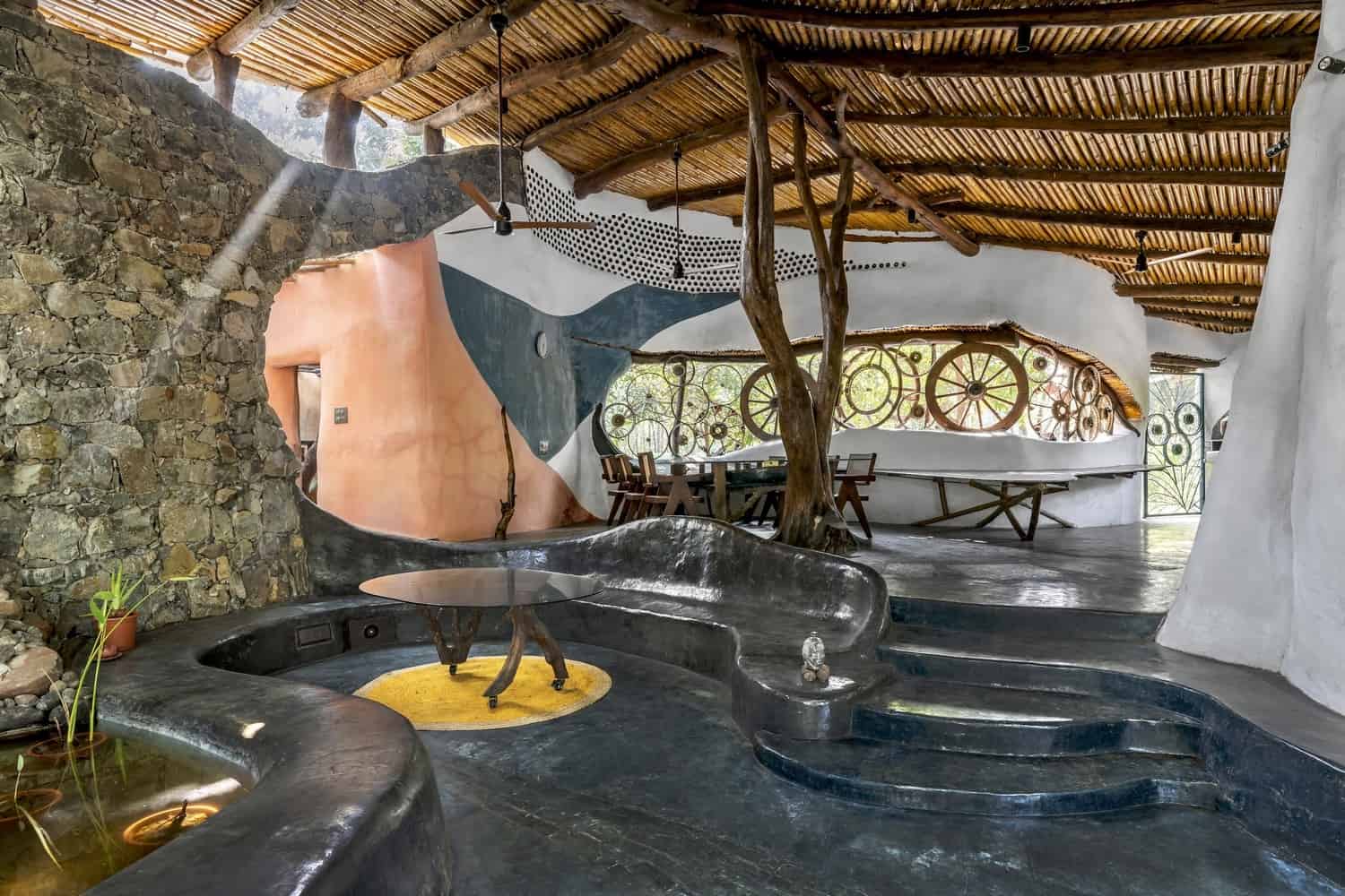 Living Pavilions Open living area with timber roof and earthen walls overlooking a shaded court.