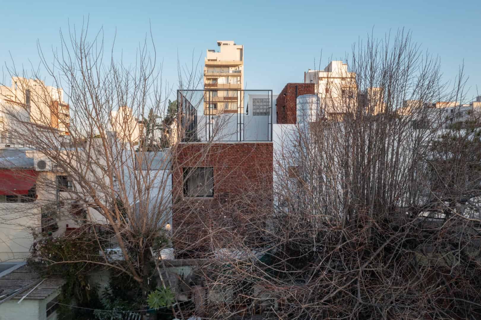 Modern urban residential architecture with mixed materials and minimalist design featuring rooftop terrace and large windows.