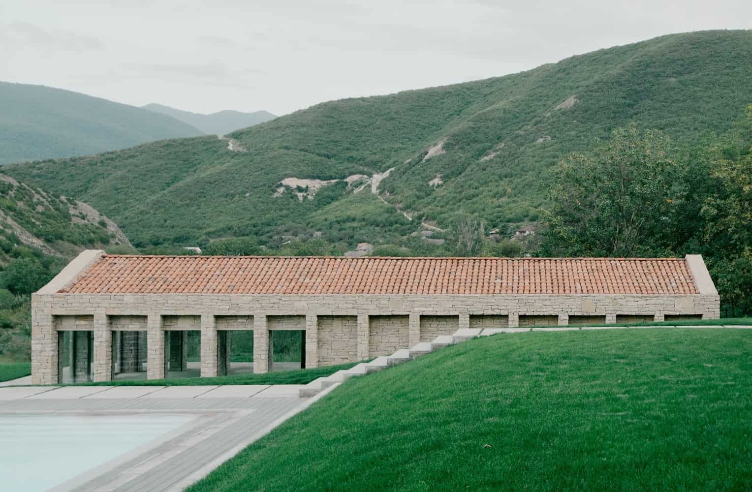 Contemporary stone building with terracotta roof in a scenic mountain landscape.
