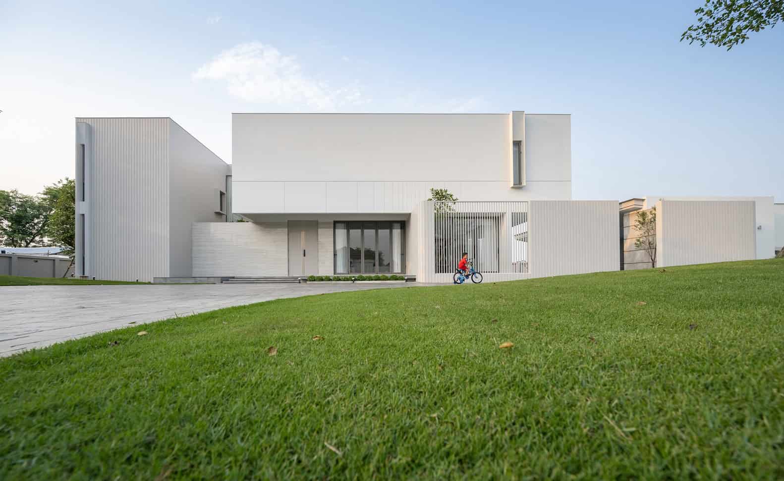 Modern minimalist white house with clean lines and contemporary architectural design, featuring a spacious lawn and a child riding a bicycle in front.