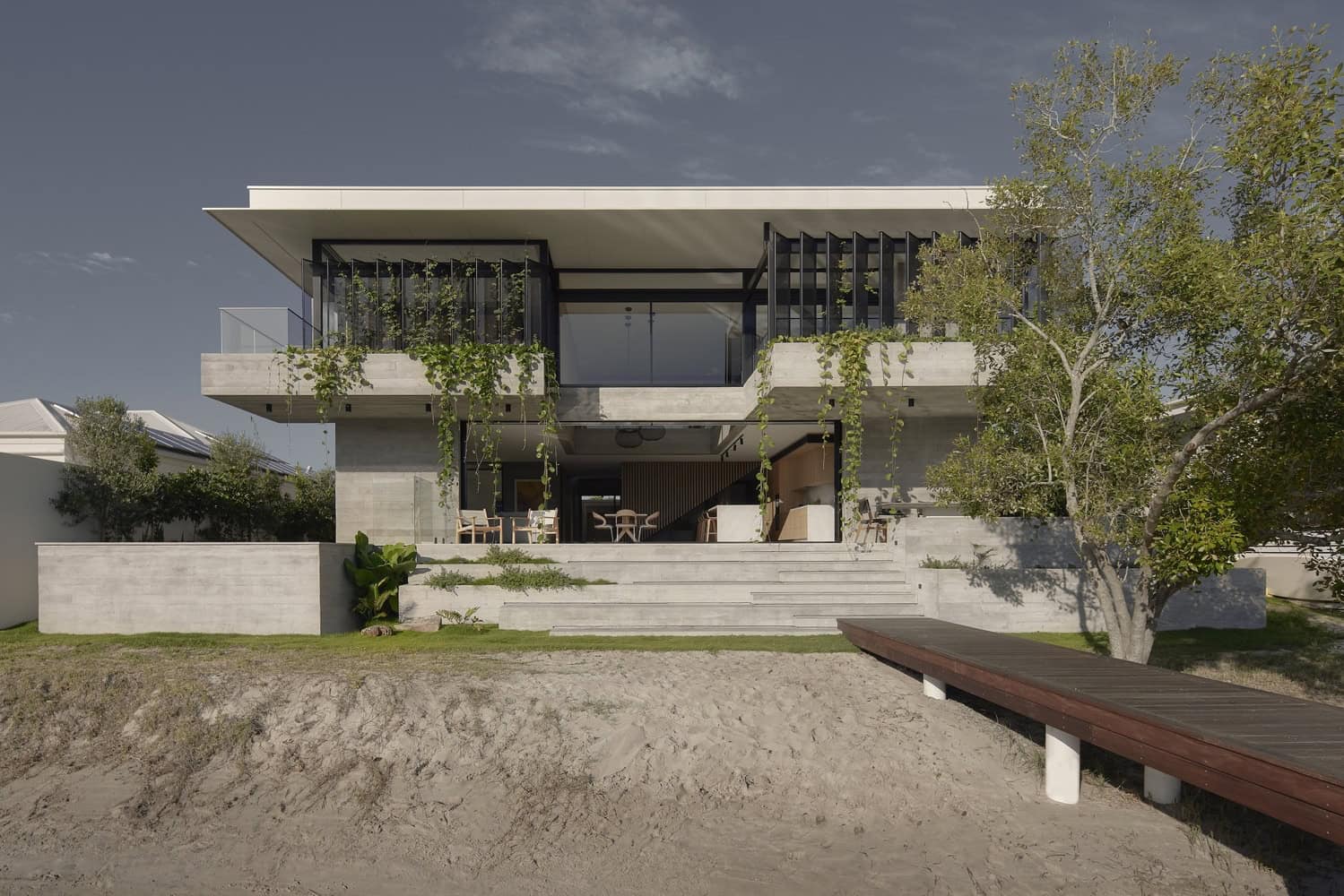Modern minimalist concrete house with large glass windows, outdoor terraces, and lush greenery, showcasing contemporary architecture and innovative design for upscale residential living.