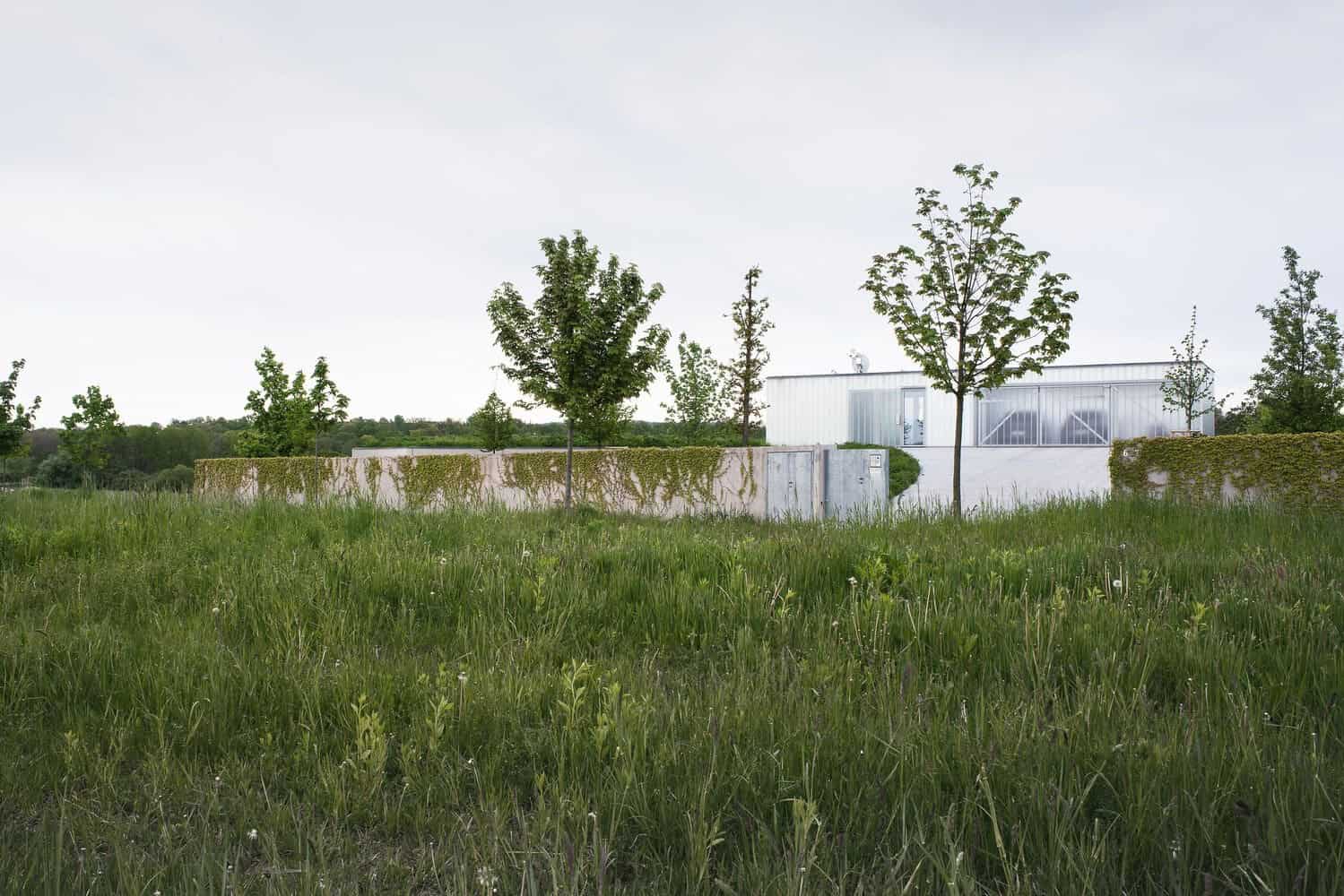 Modern minimalist white house with geometric architecture and large glass windows amidst lush green landscape.