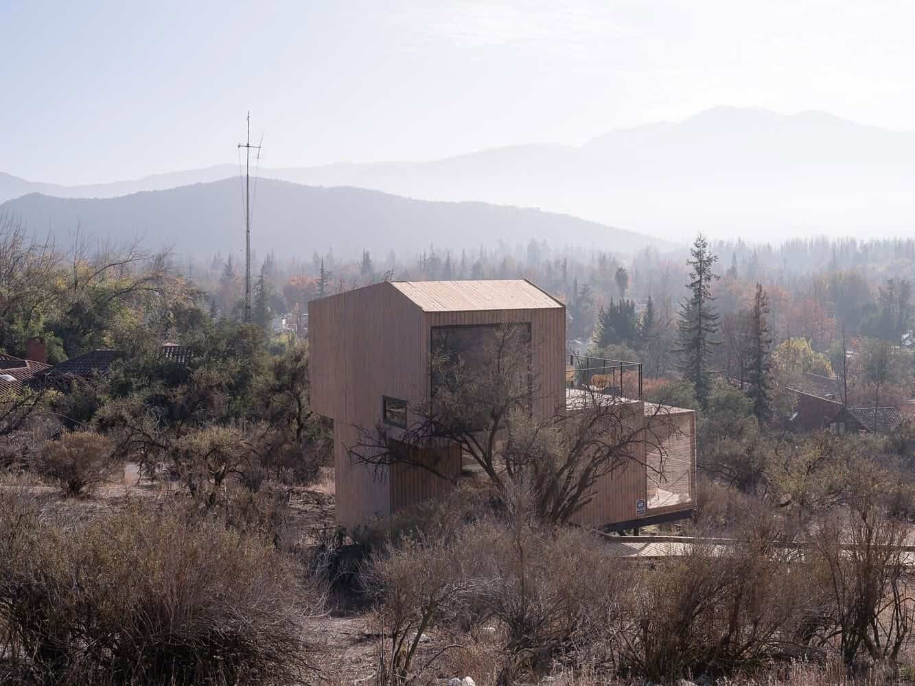 Sustainable modern tiny house built with natural wood in a serene woodland environment amidst trees and mountains.