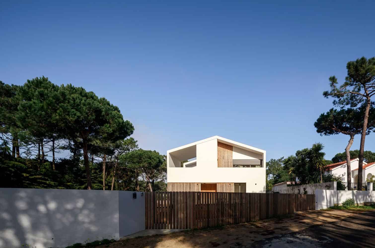 Modern minimalist white house with wooden accents surrounded by lush trees and clear blue sky.