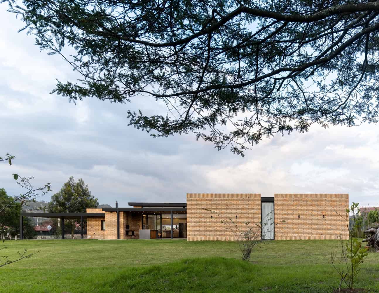 Contemporary modern house with minimalist design and brick exterior, surrounded by lush green lawn and trees, showcasing innovative architecture and stylish outdoor living space.
