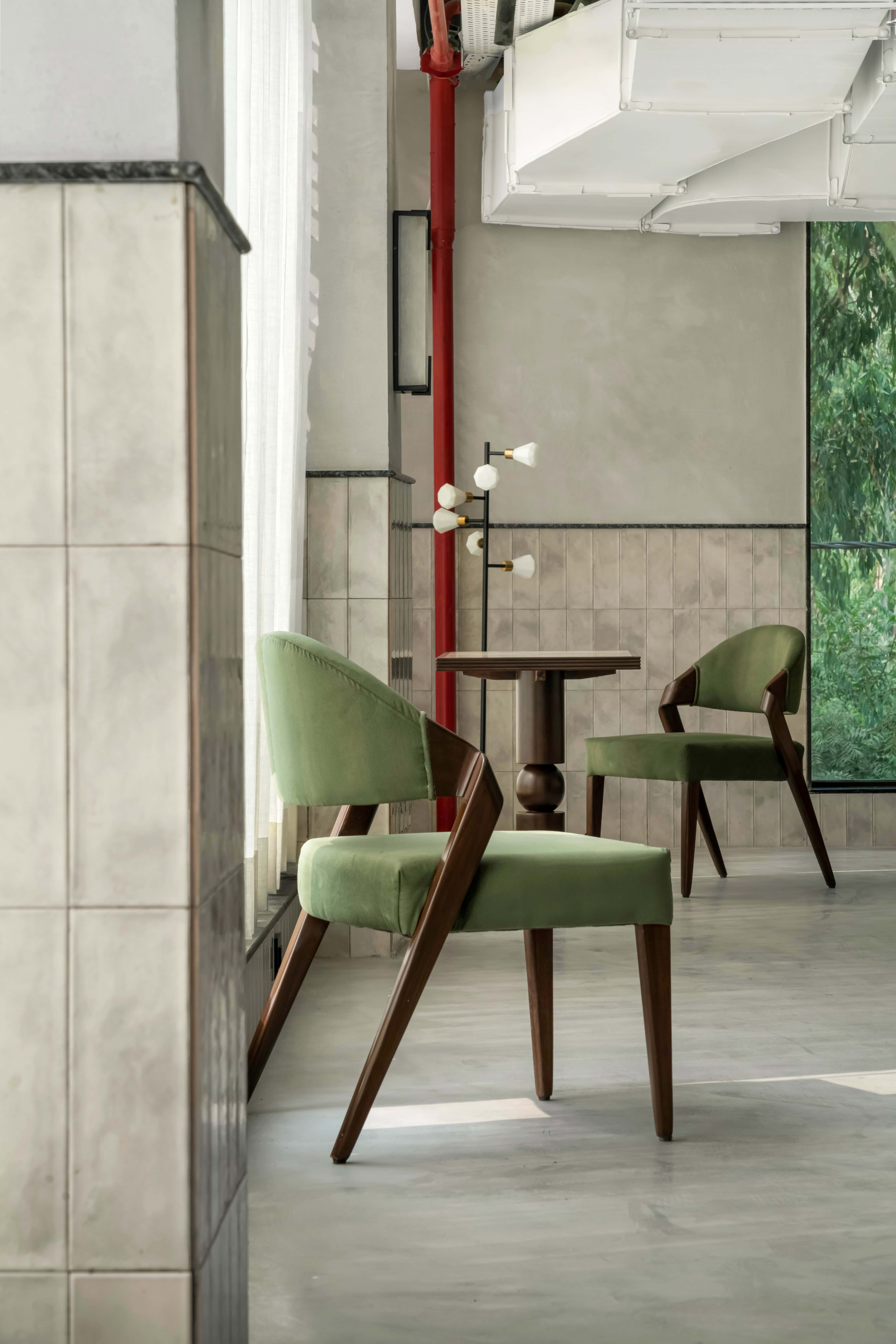 Modern interior design with green velvet chairs, wooden accents, and contemporary lighting for stylish home decor.