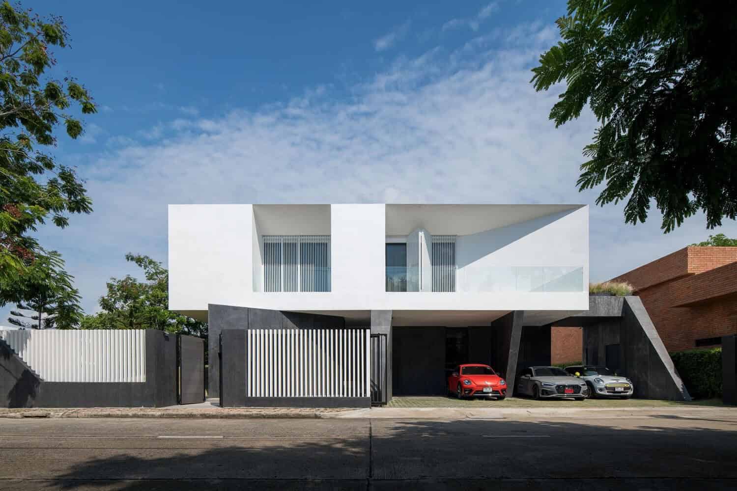 Modern minimalist house with geometric design and sleek white exterior, featuring clean lines and large windows, set amidst lush greenery and contemporary architecture.