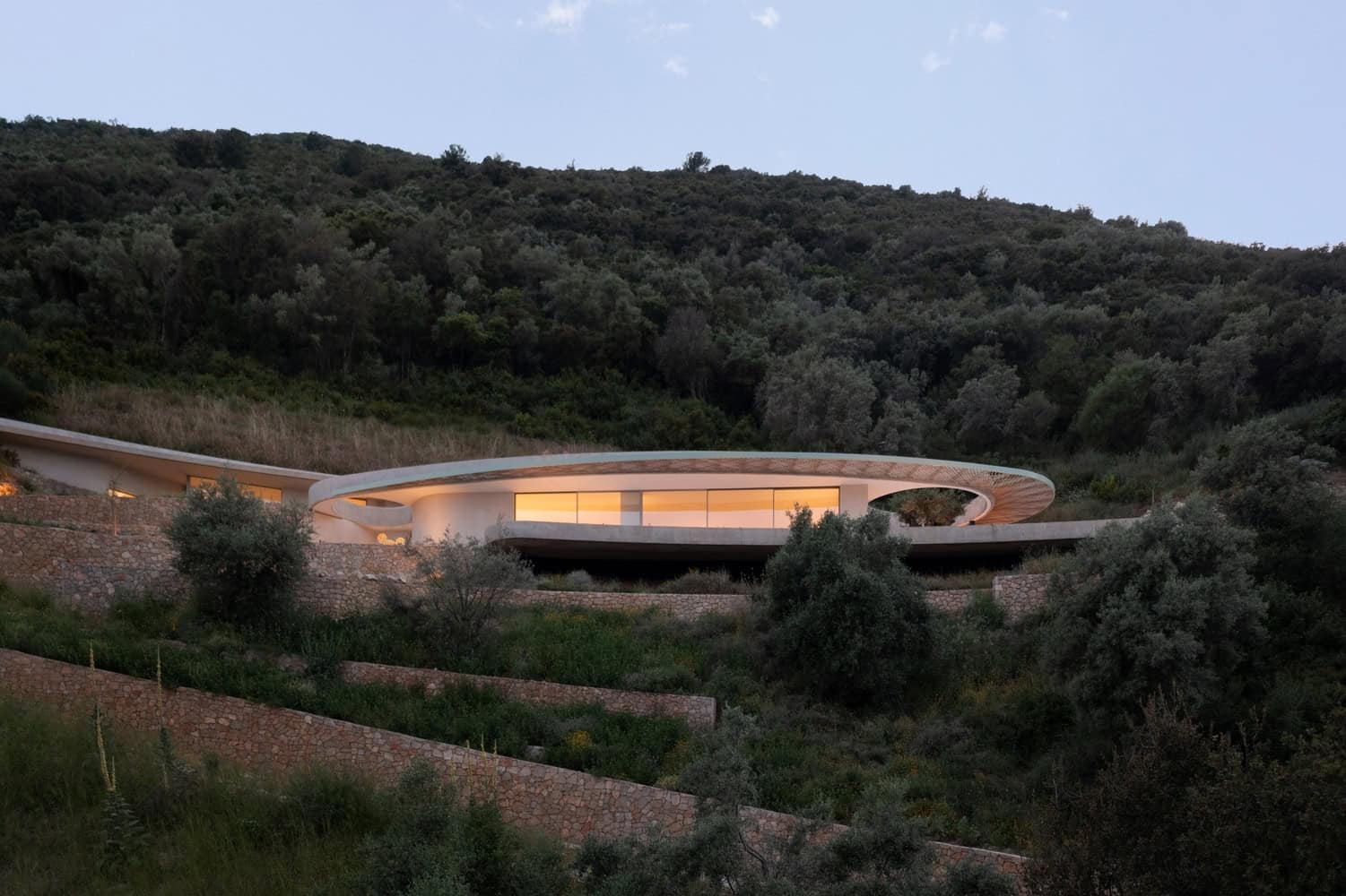 Modern hillside house with sleek architectural design nestled among lush greenery, featuring curved lines and large glass windows, exemplifying contemporary architecture art and design.