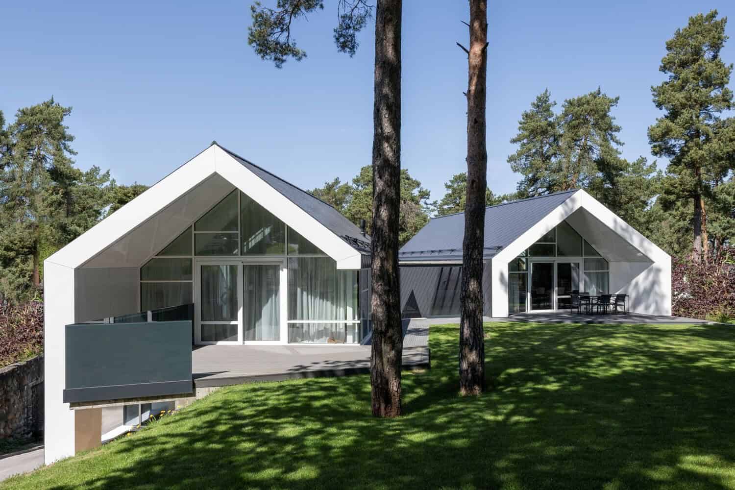 Contemporary minimalist house with pitched roofs and large glass windows in a forest setting.