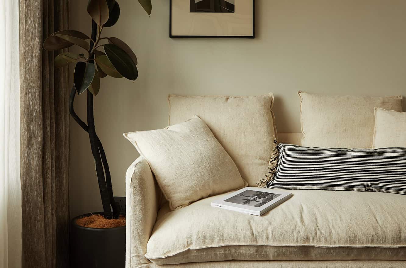 Soothing beige sofa with decorative pillows in a modern living room with a potted plant and framed artwork on the wall, showcasing contemporary interior design and cozy home decor elements.