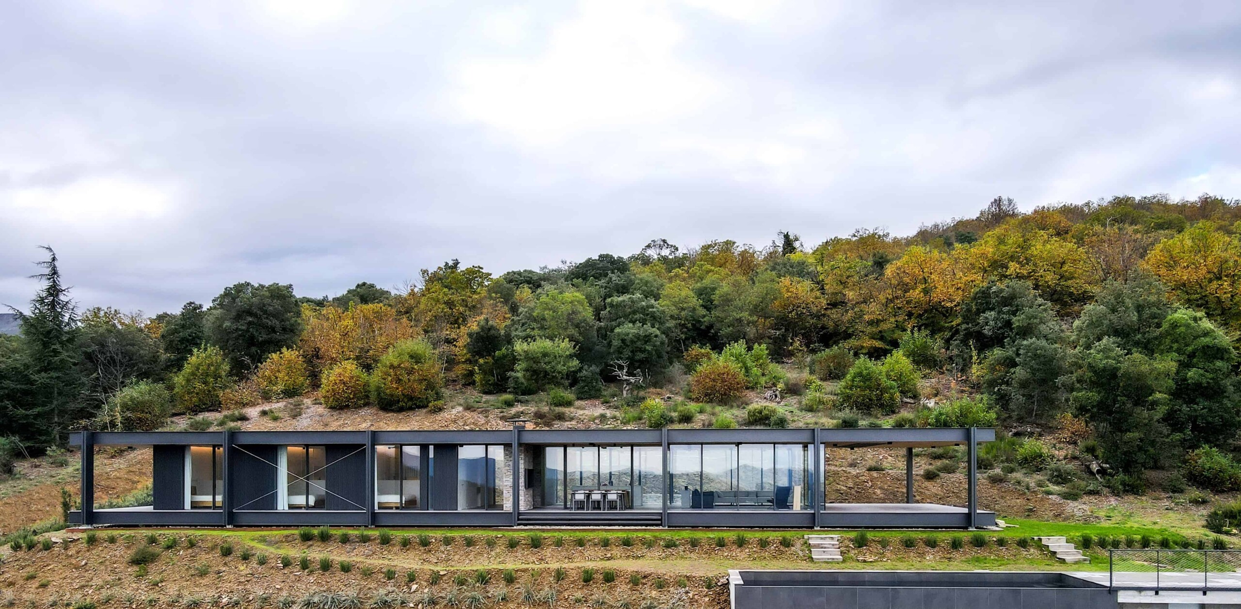 Contemporary minimalist glass house with modern architecture, sleek design, and expansive windows nestled in a natural hillside environment.