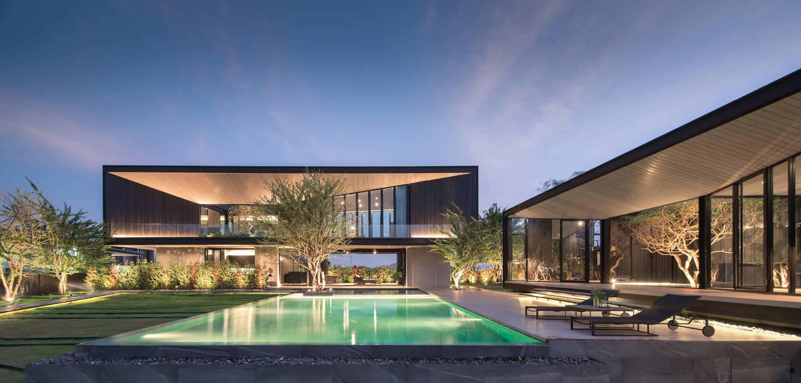 Sleek modern luxury house with glass walls, outdoor pool, and landscaped garden at dusk, showcasing contemporary architectural design and stylish outdoor living space.