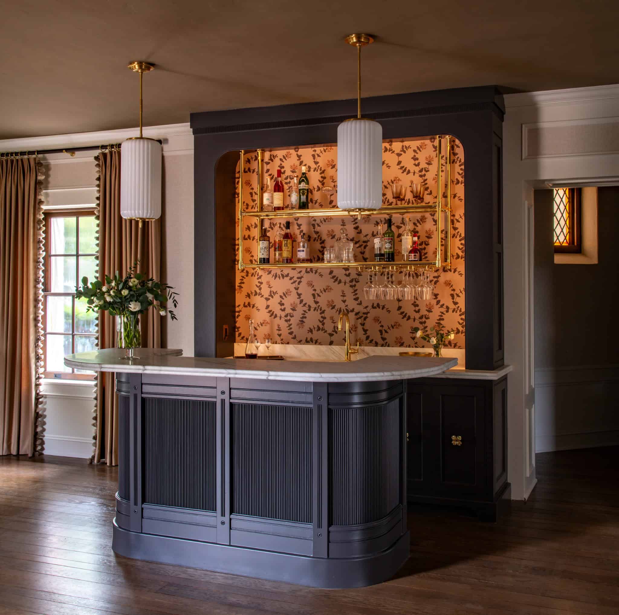 Bauer Lounge Modern Bar Design Elegant bar nook with gold shelving, floral wallpaper, and navy paneling at the Bauer Lounge.