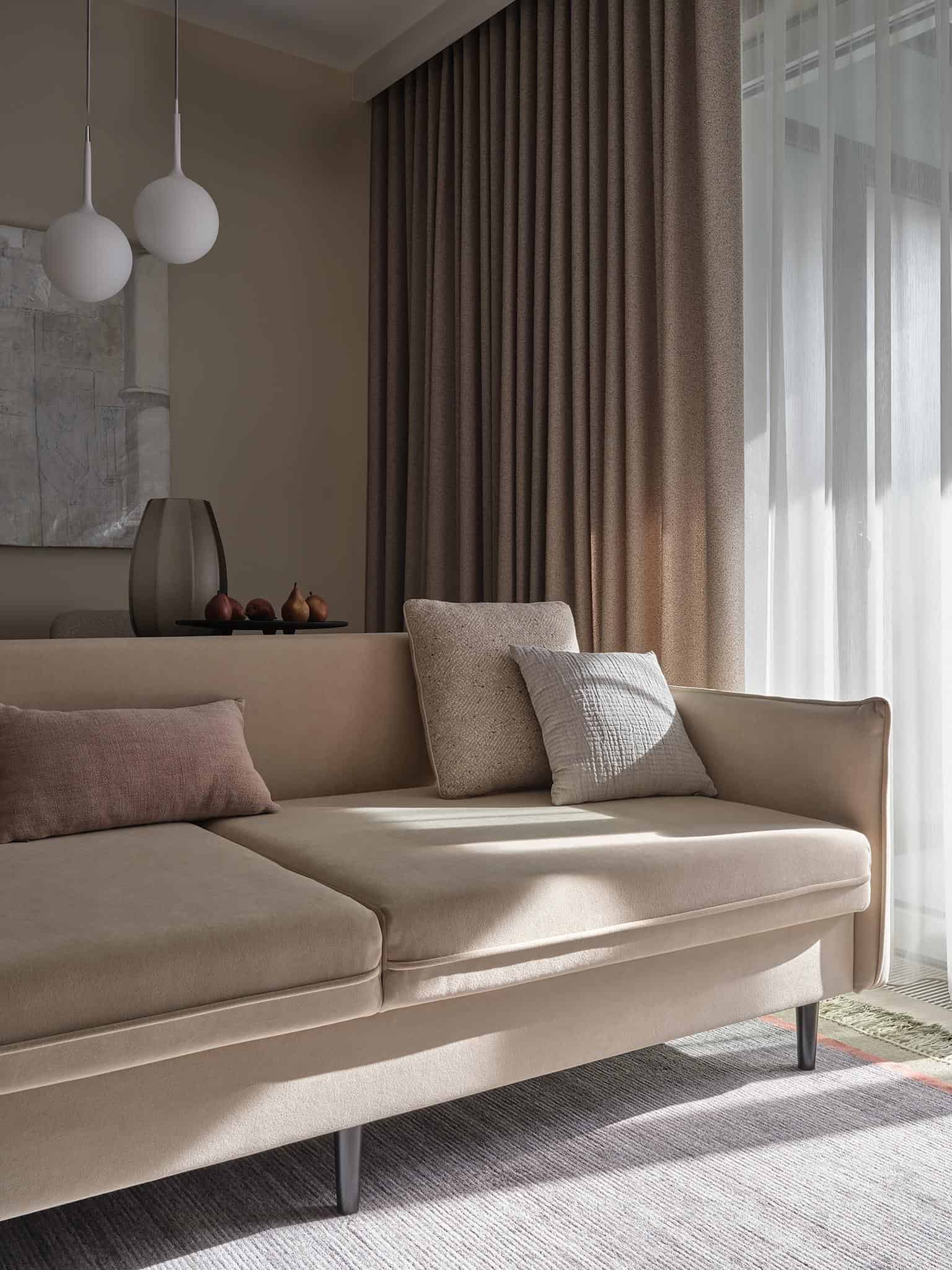 Beige Apartment Sofa and Curtains Closeup Close-up of beige sofa with brown throw and floor-to-ceiling curtains in a neutral living room.