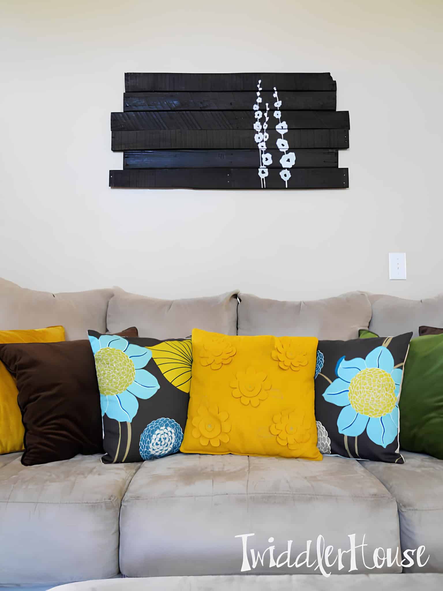 Black wooden slat artwork with white flower silhouettes mounted above a beige couch.