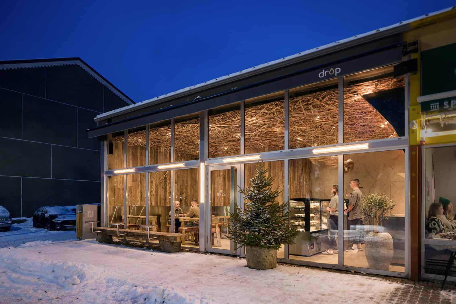 Coffee Shop Kovel Night Glass Facade Full glass facade view of coffee shop with patrons and tree-lined snowy walkway