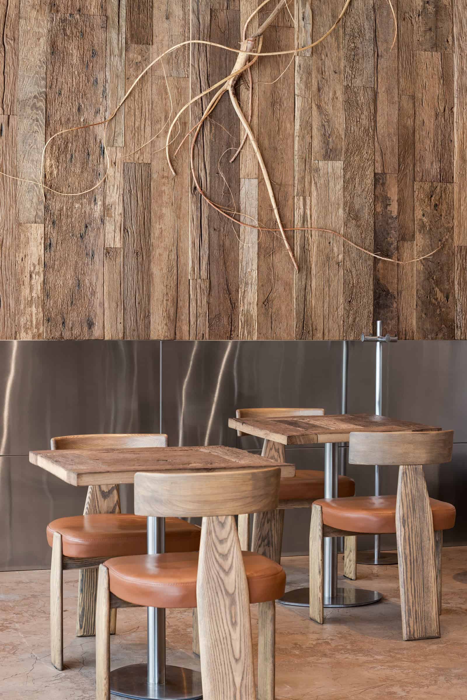 Coffee Shop Kovel Rustic Wooden Tables Square rustic wood tables and round leather seats inside a warm-toned coffee shop
