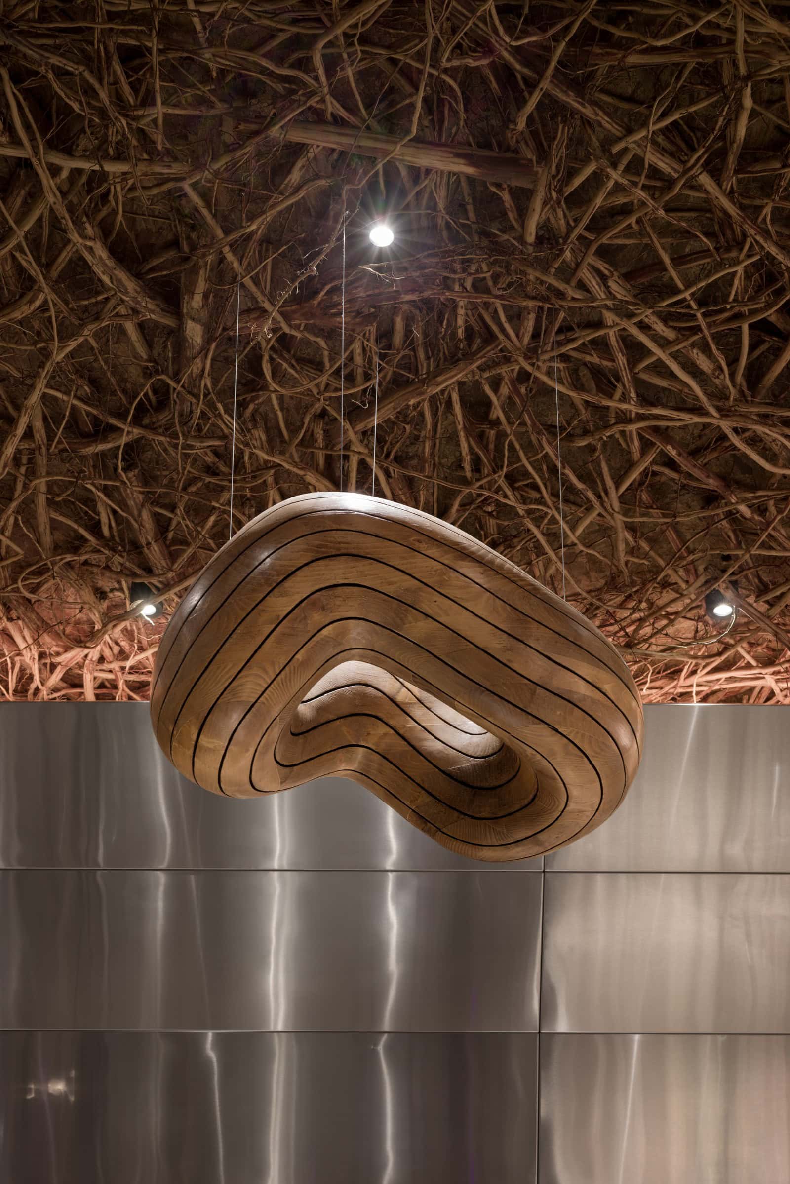 Coffee Shop Kovel Sculptural Wood Light Organic-shaped wooden lamp hanging beneath rustic twig ceiling
