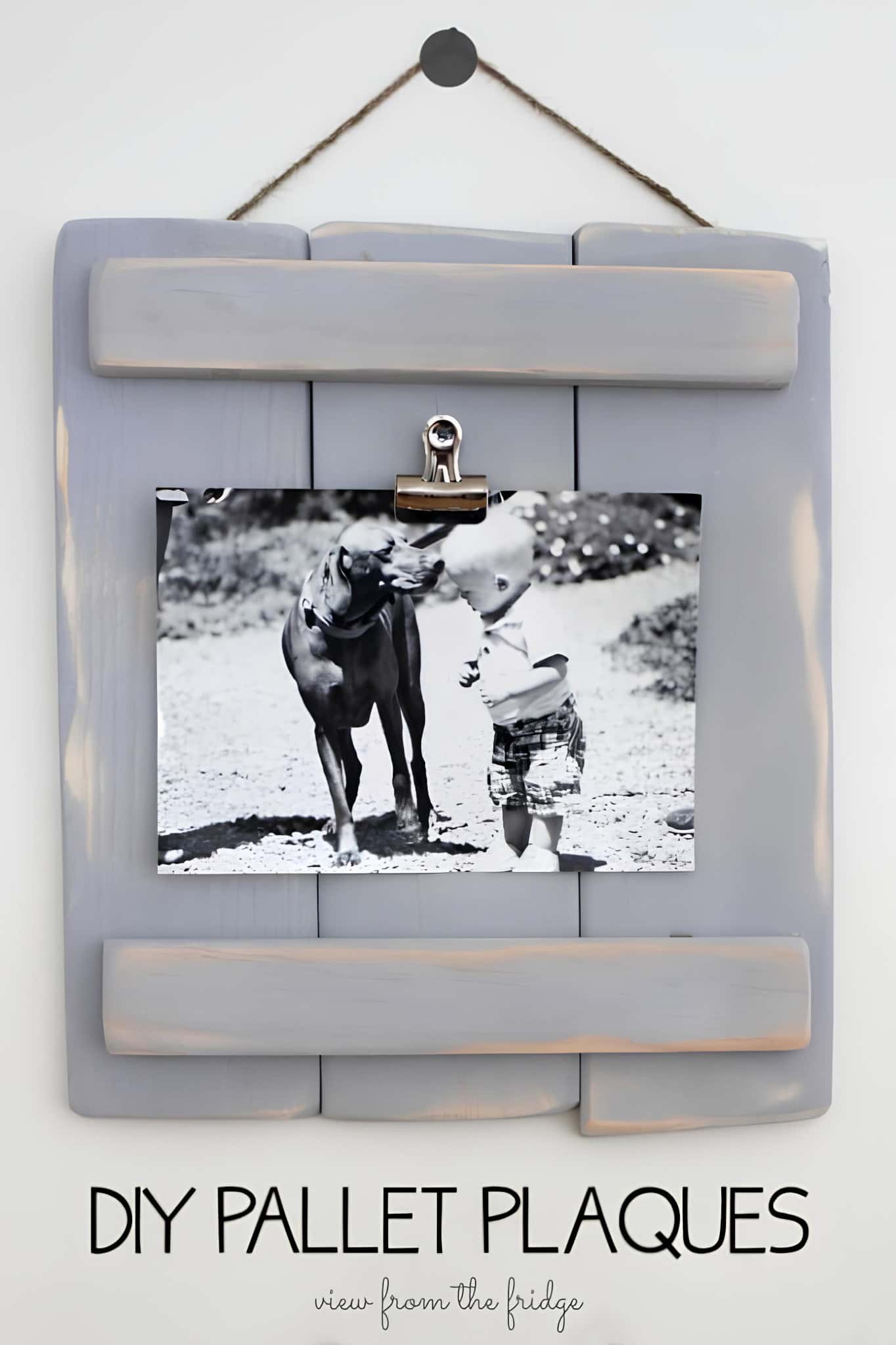 Gray painted wood plaque with clip holding a black and white photo, hung with twine.