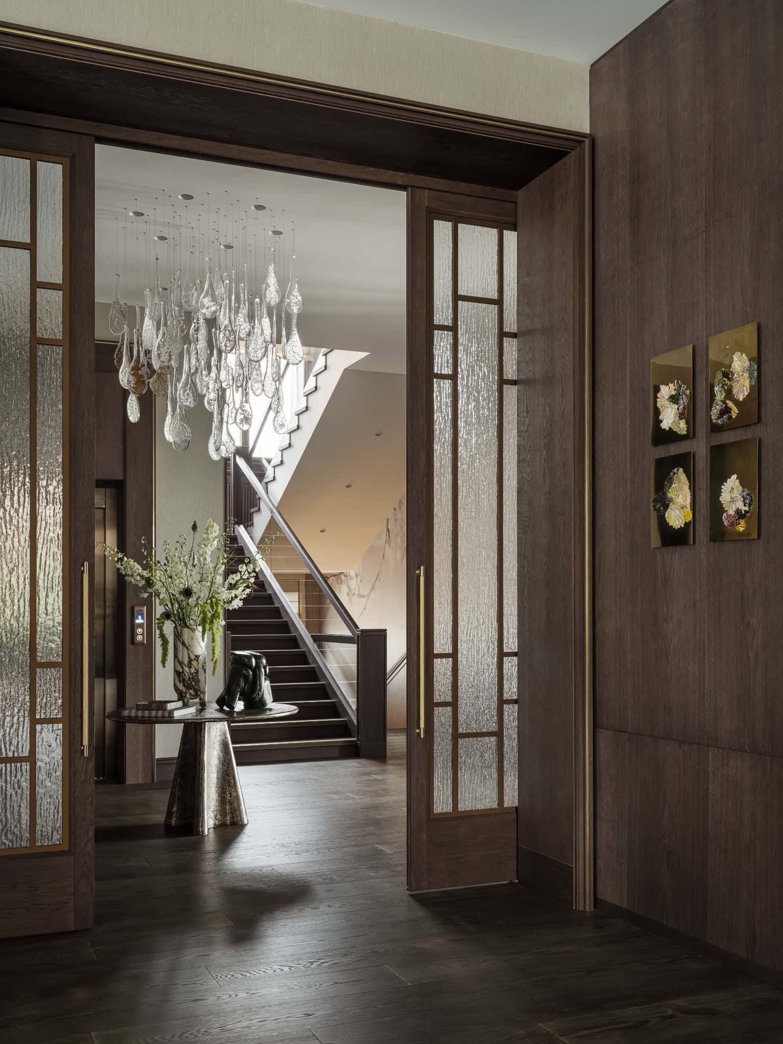Entryway with Glass Doors and Sculptural Light View of the foyer through glass doors with artistic chandelier and round table.