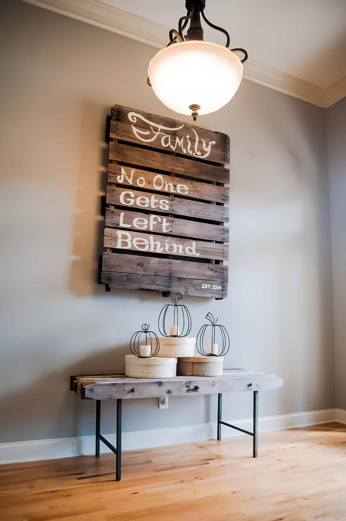 Rustic wood pallet wall decor with quote 'Family No One Gets Left Behind' and decorative pumpkins below.