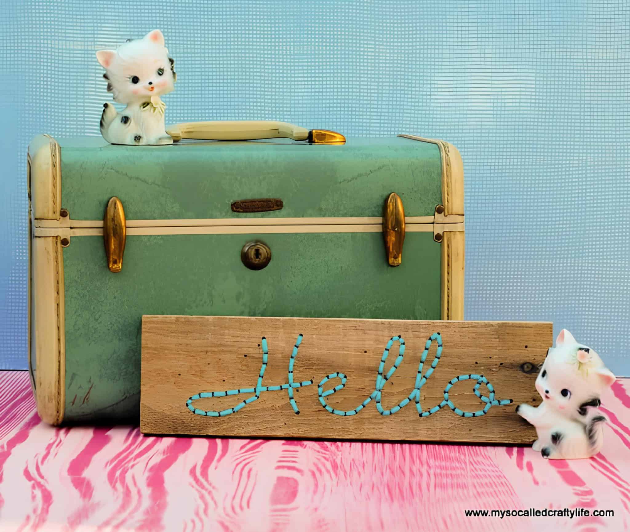Small wooden sign with the word 'Hello' created using turquoise string art, beside retro decor.