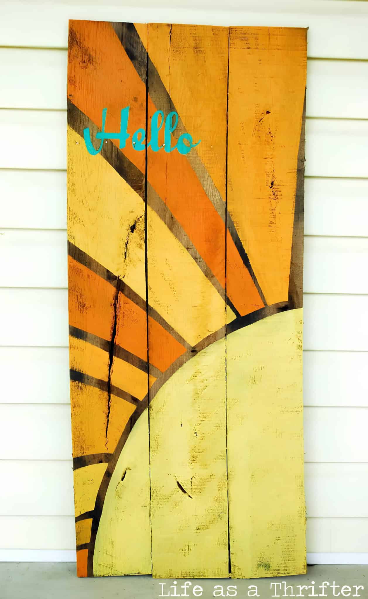 Vertical pallet board art with painted yellow and orange sun rays and 'Hello' text.