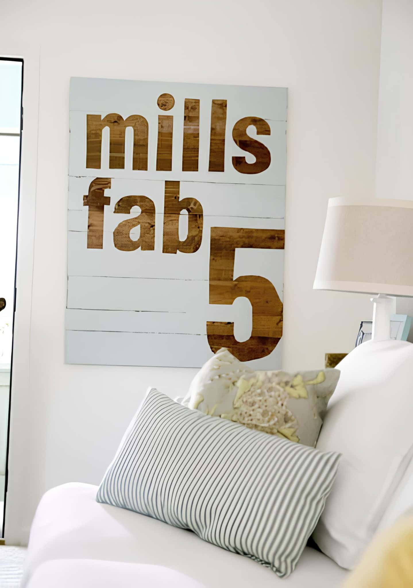 Modern farmhouse-style wooden sign with the words 'mills fab 5' above a white sofa.