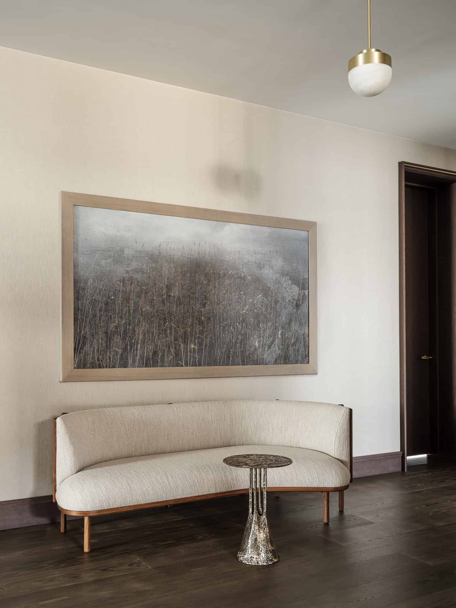 Minimal Sofa Seating Beside Wall Art Curved light sofa with modern brass side table beneath textured painting.